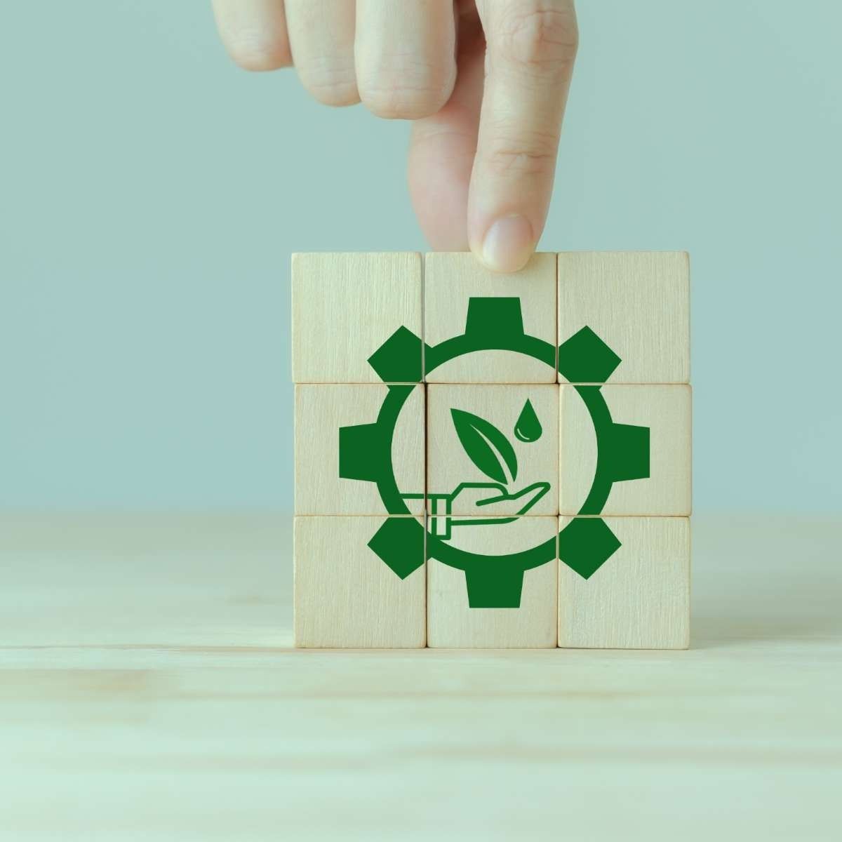 Una mano sostiene un bloque de madera con un engranaje verde y un icono de hoja sobre él.