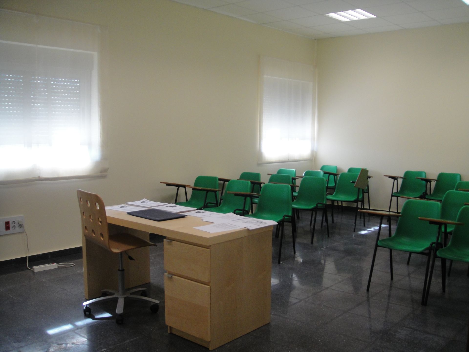 Un aula con sillas verdes y un escritorio.