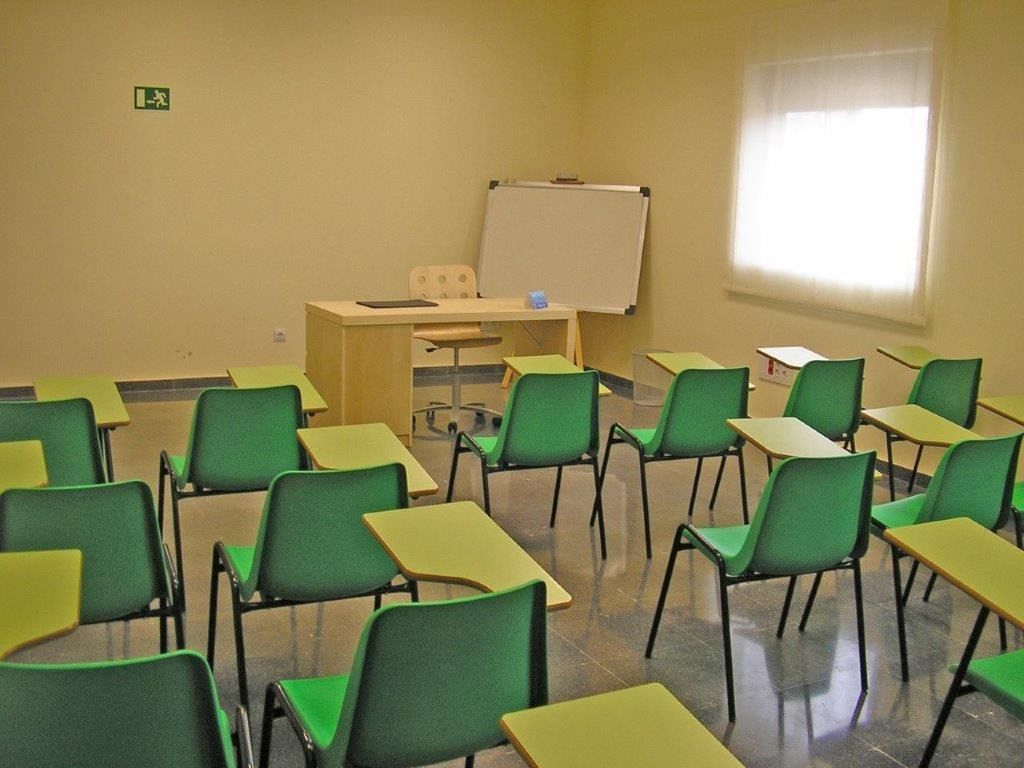 Un aula con sillas verdes y escritorios amarillos.