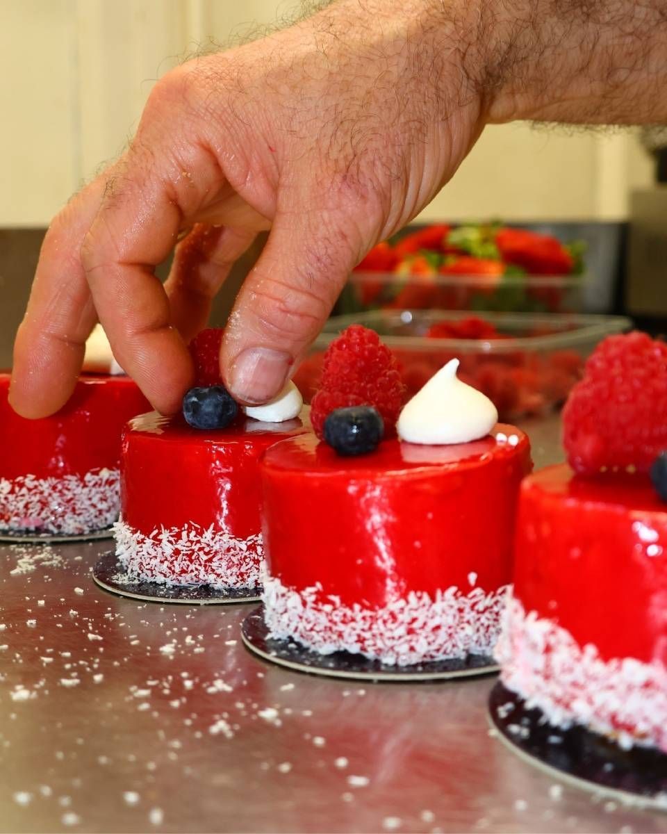 Déposer à la main des baies sur de petits desserts rouges saupoudrés de noix de coco, présentés sur un plateau.