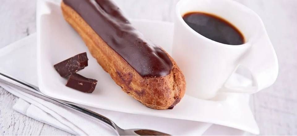 Éclair au chocolat et tasse de café sur une assiette blanche avec un fond de journal
