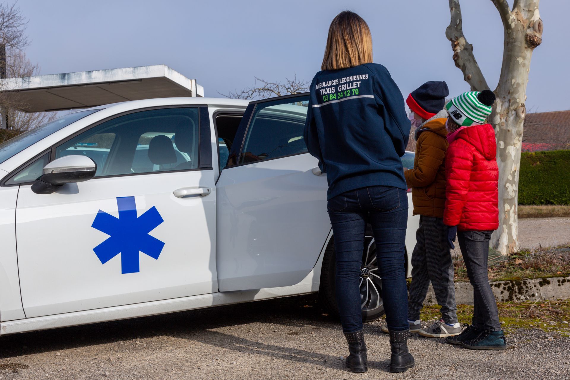 Une conductrice de VSL ouvrant la porte du véhicule à deux enfants.