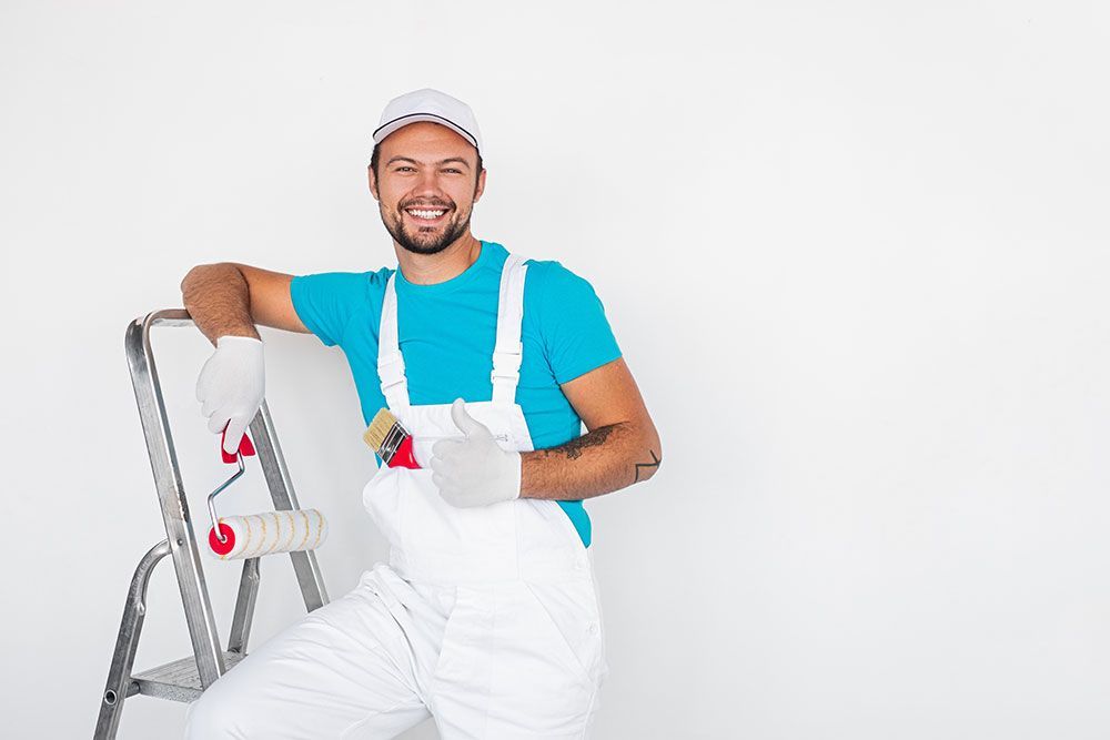 Ein Mann lehnt an einer Leiter und hält eine Farbrolle.