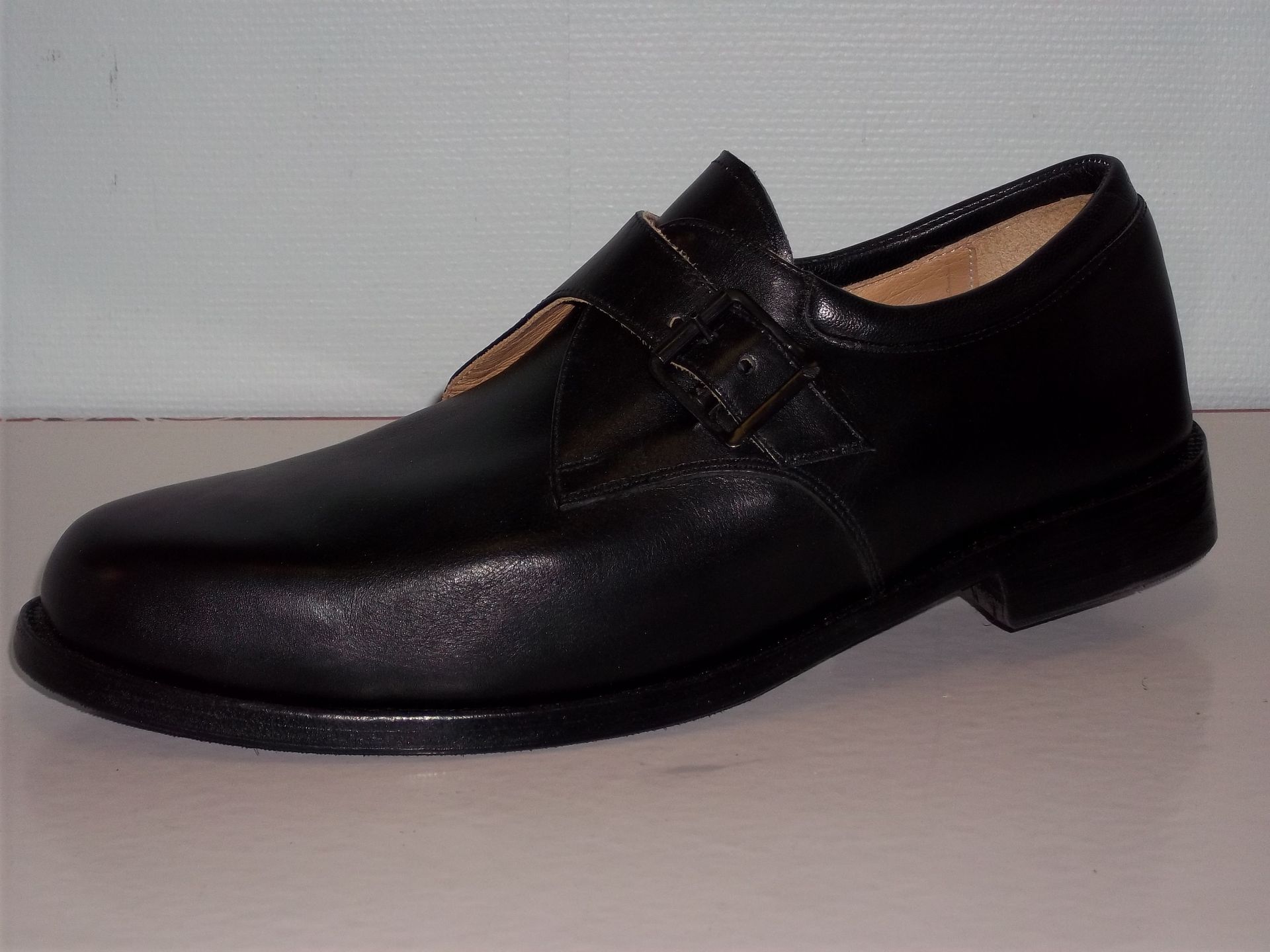 Chaussure habillée en cuir noir à petit talon, vue de profil sur fond uni