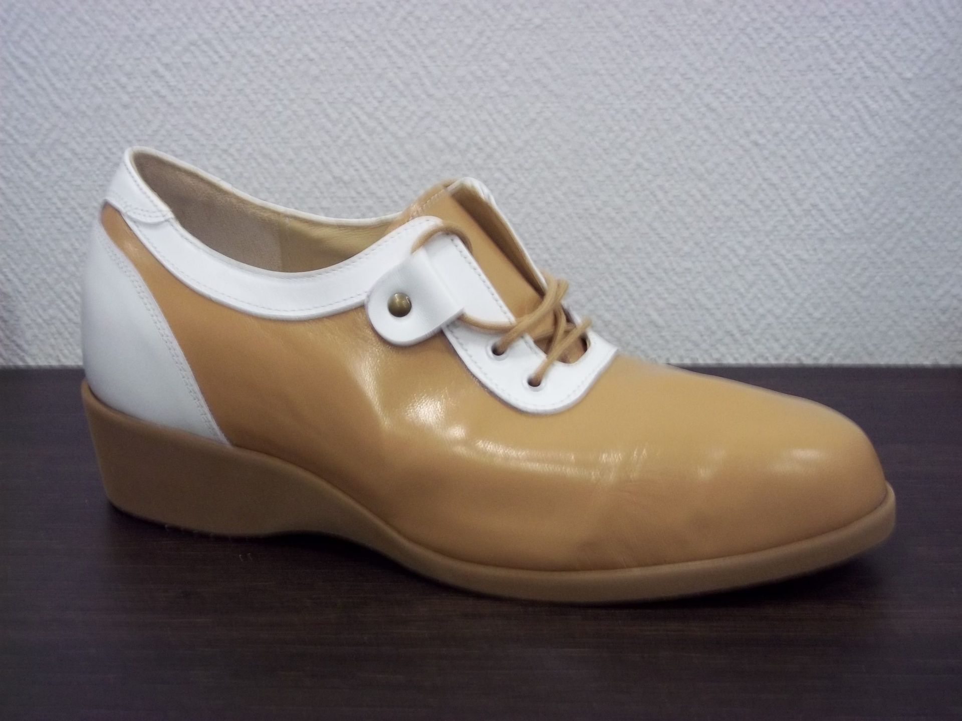 Chaussure Oxford en cuir fauve avec détails blancs et petit talon compensé sur une surface foncée