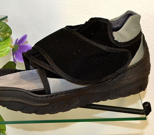 Baskets montantes noires et grises présentées sur une étagère en verre avec une fleur violette à côté.