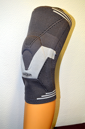 Genouillère grise sur une jambe orange contre un mur texturé.