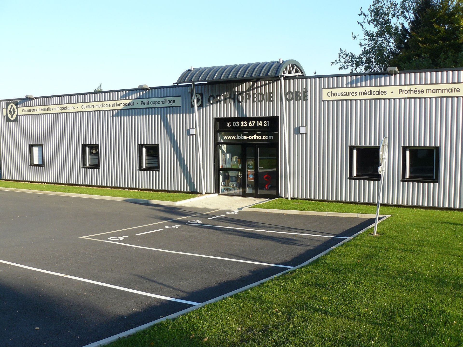 Petit bâtiment industriel avec bardage en tôle ondulée grise, entrée vitrée et parking vide devant.