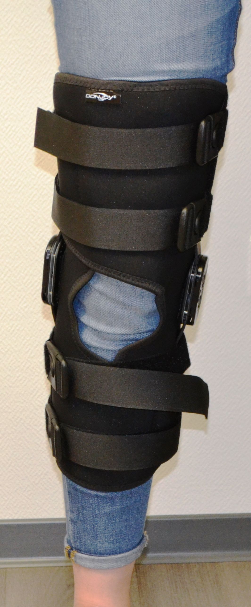 Personne portant une genouillère noire par-dessus un jean bleu et une basket blanche à une jambe