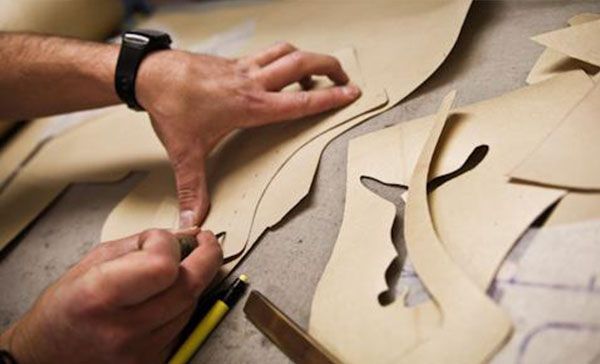 Des mains découpant des patrons de tissu beige avec des ciseaux et une règle sur une table de travail