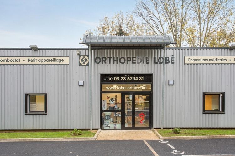 Façade de clinique orthopédique avec bardage gris, porte centrale vitrée et enseignes indiquant ORTHOPEDIE LOBE