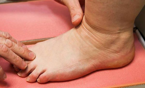 Des mains massent une cheville et un pied sur un tapis rose