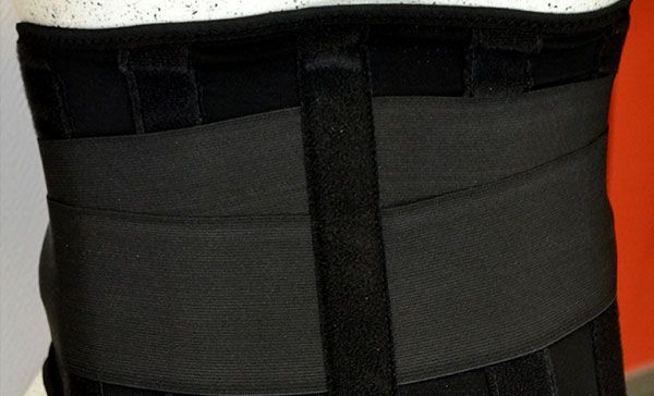 Ceinture de soutien lombaire noire avec larges panneaux avant et sangles verticales sur fond blanc et orange