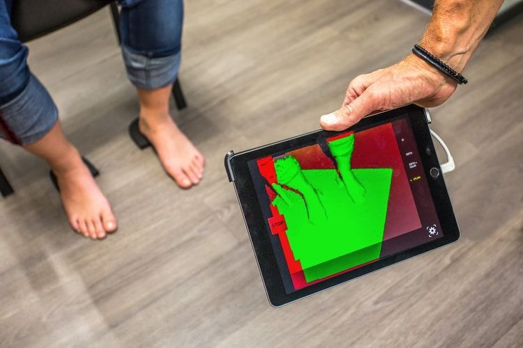 Deux personnes se tiennent près d'une tablette affichant une superposition de scan verte et rouge sur le sol.