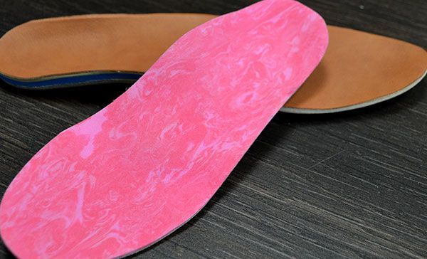 Semelle intérieure rose avec une semelle extérieure beige et noire sur une surface en bois foncé.