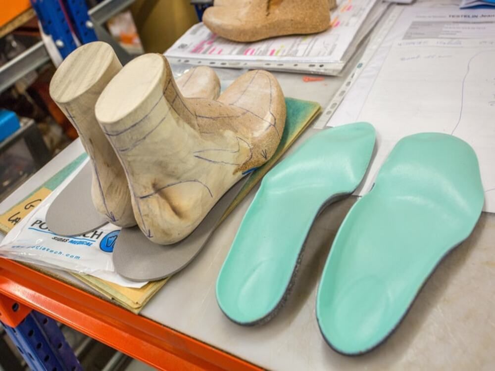Forme à chaussures en bois et semelles orthopédiques vert menthe sur une table de travail avec des papiers et des outils