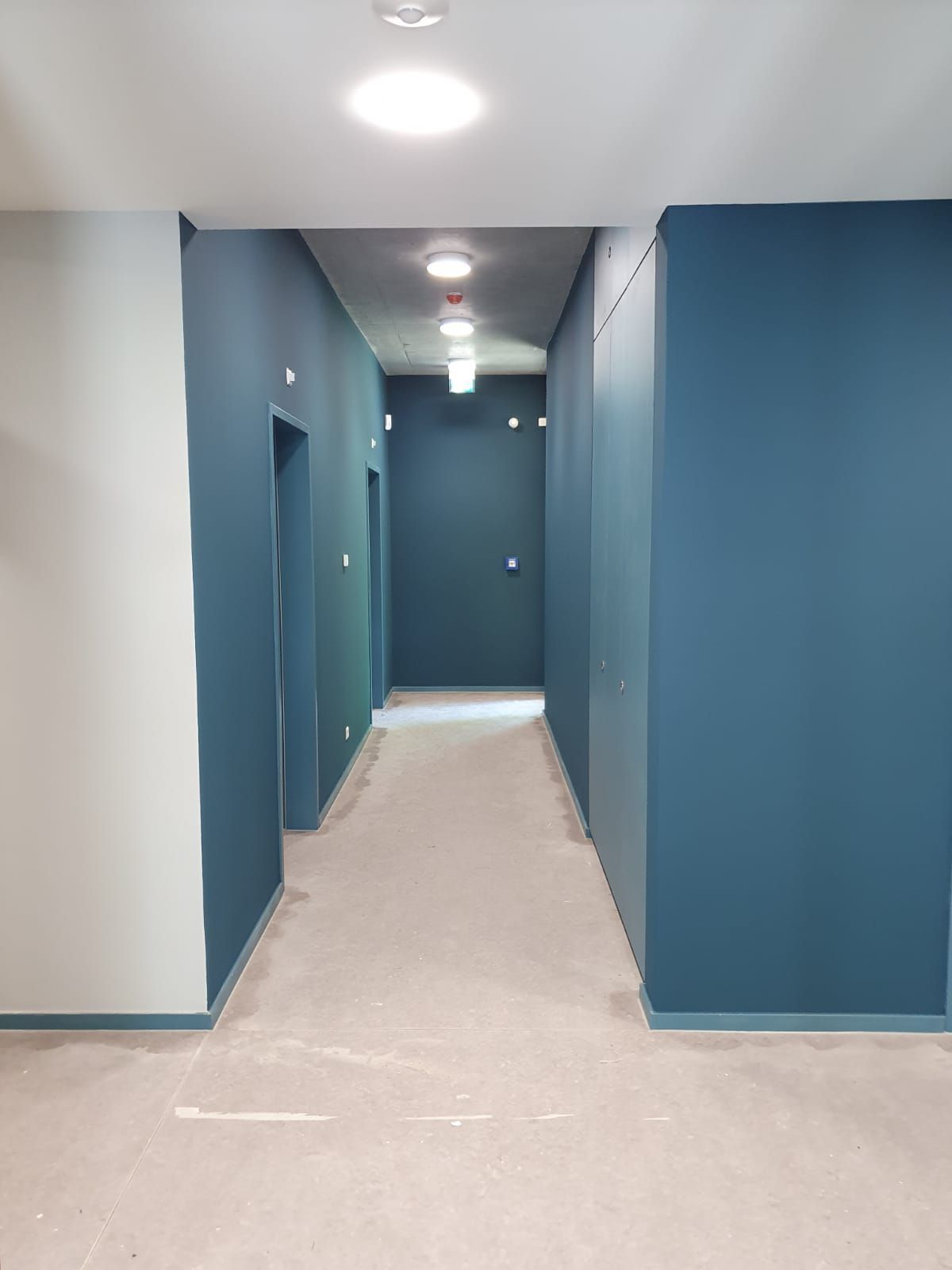 Ein langer Flur mit blauen Wänden und Deckenbeleuchtung.