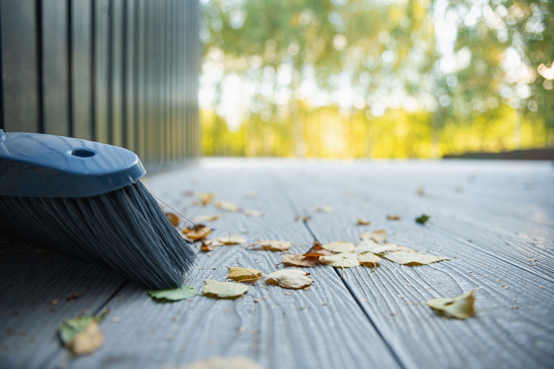 Balai posé sur une terrasse en bois gris avec des feuilles mortes