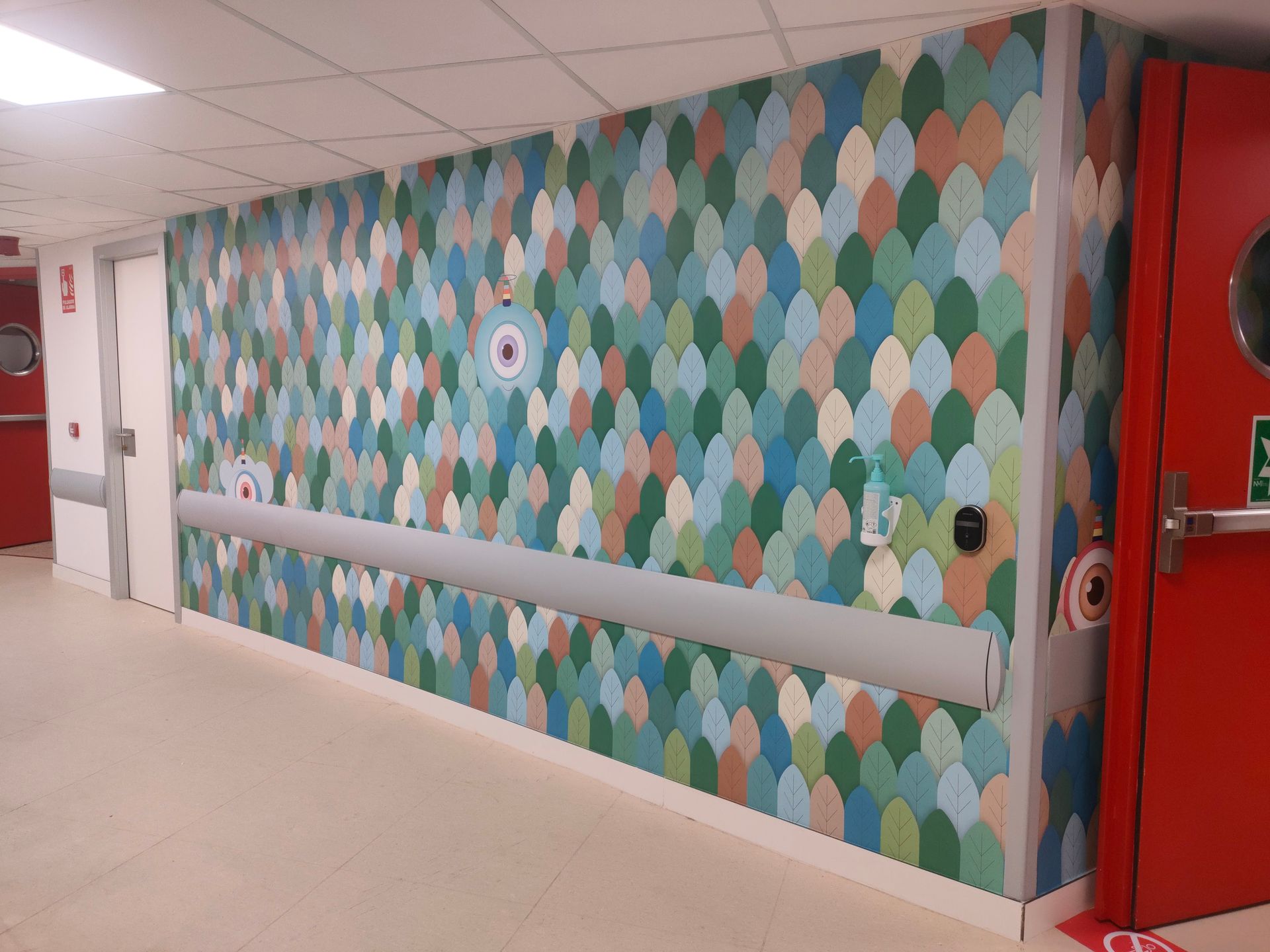 Un pasillo con una pared colorida y una puerta roja.