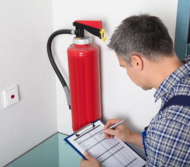 Un hombre está escribiendo en un portapapeles al lado de un extintor de incendios.