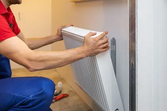 Un hombre está instalando un radiador en una pared.