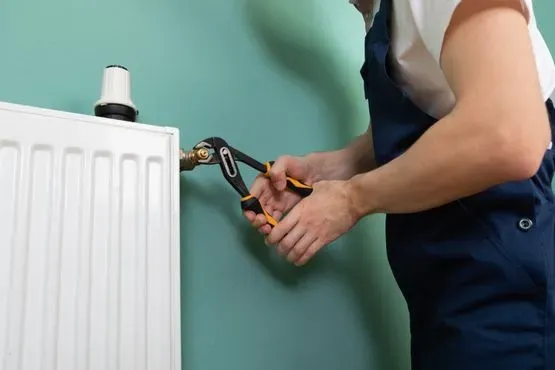 Un hombre está arreglando un radiador con una llave inglesa.