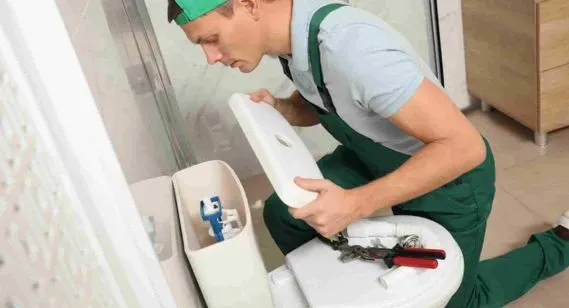 Un hombre está arreglando un inodoro en un baño.