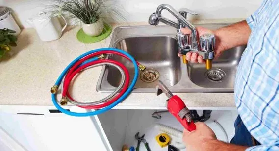 Un fontanero está arreglando un grifo en un fregadero de cocina.