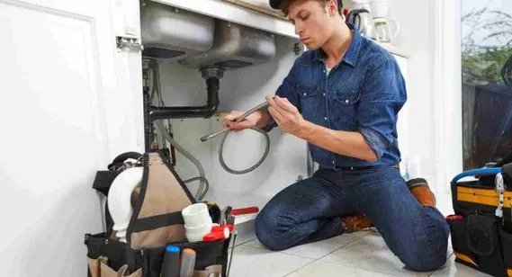 Un fontanero está arrodillado en el suelo arreglando un fregadero.
