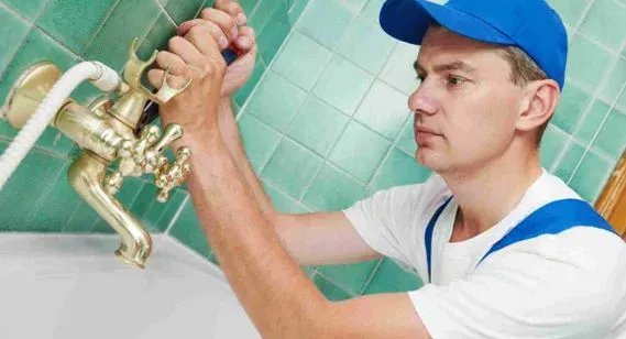 Un hombre está arreglando un grifo en un baño.