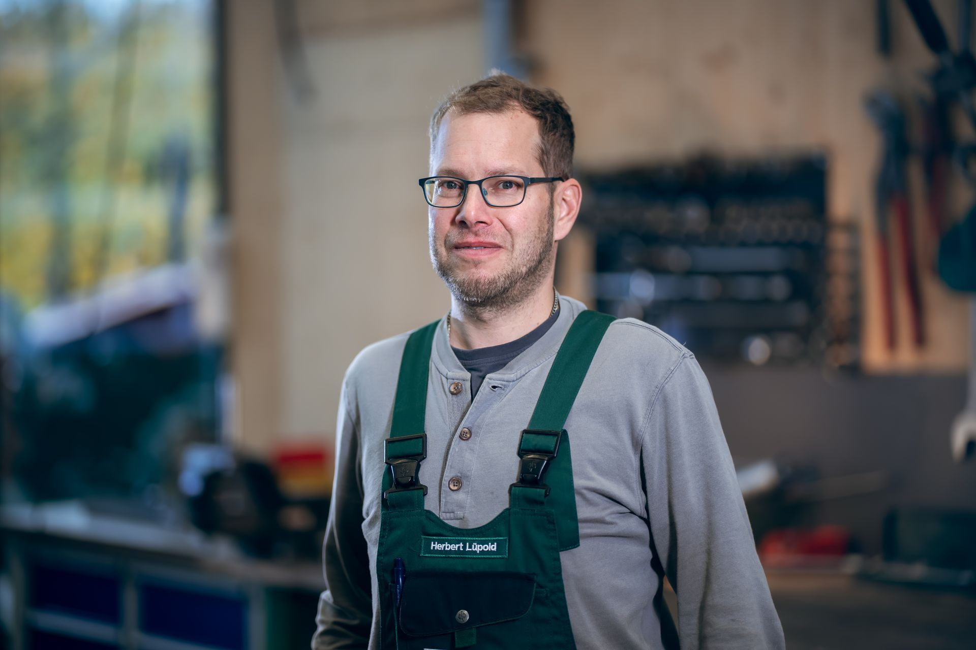 Ein Mechaniker arbeitet in einer Werkstatt an einem orangefarbenen Traktor und liegt dabei auf dem Boden.