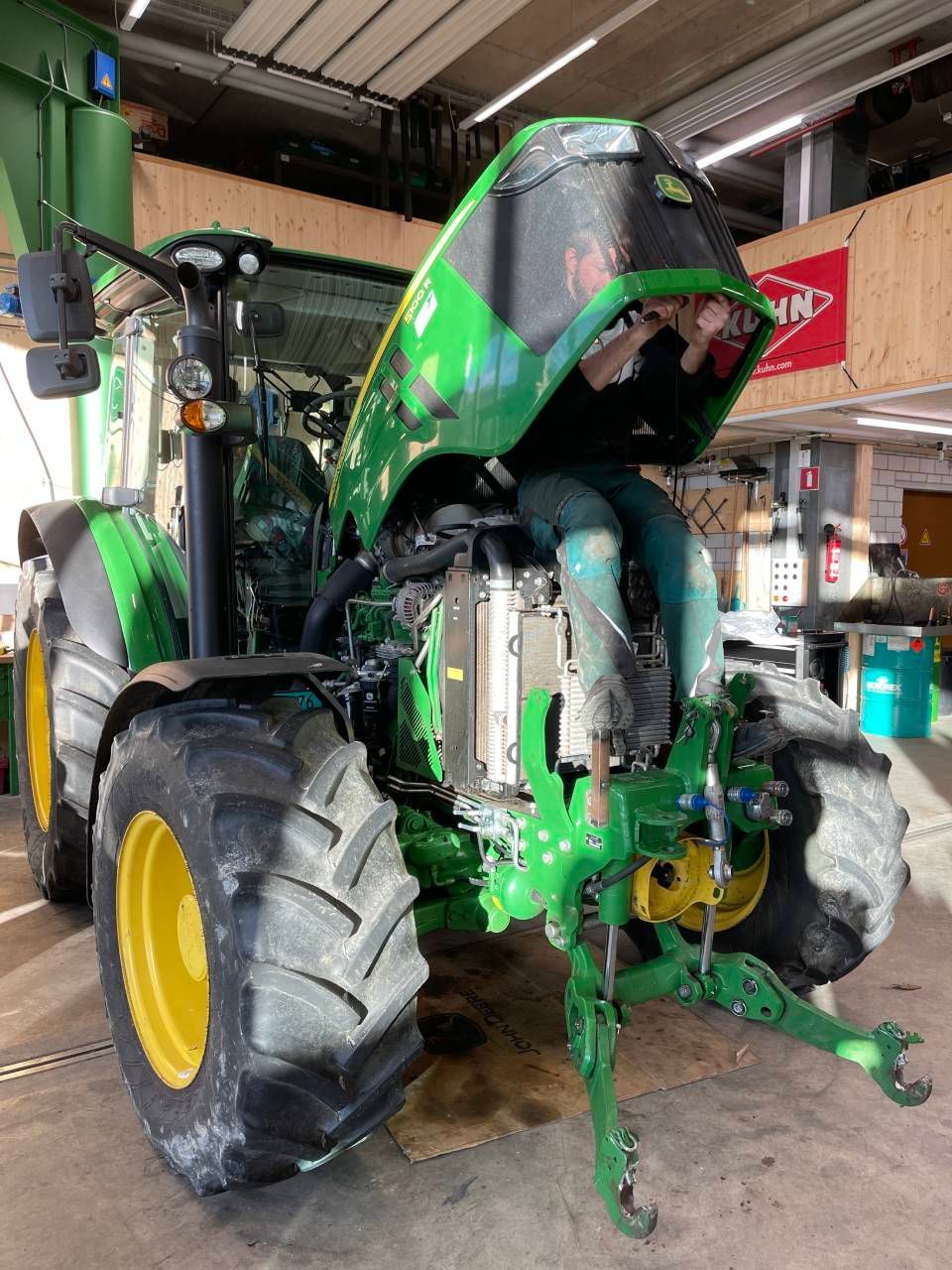 Ein Mechaniker arbeitet in einer Werkstatt an einem orangefarbenen Traktor und liegt dabei auf dem Boden.