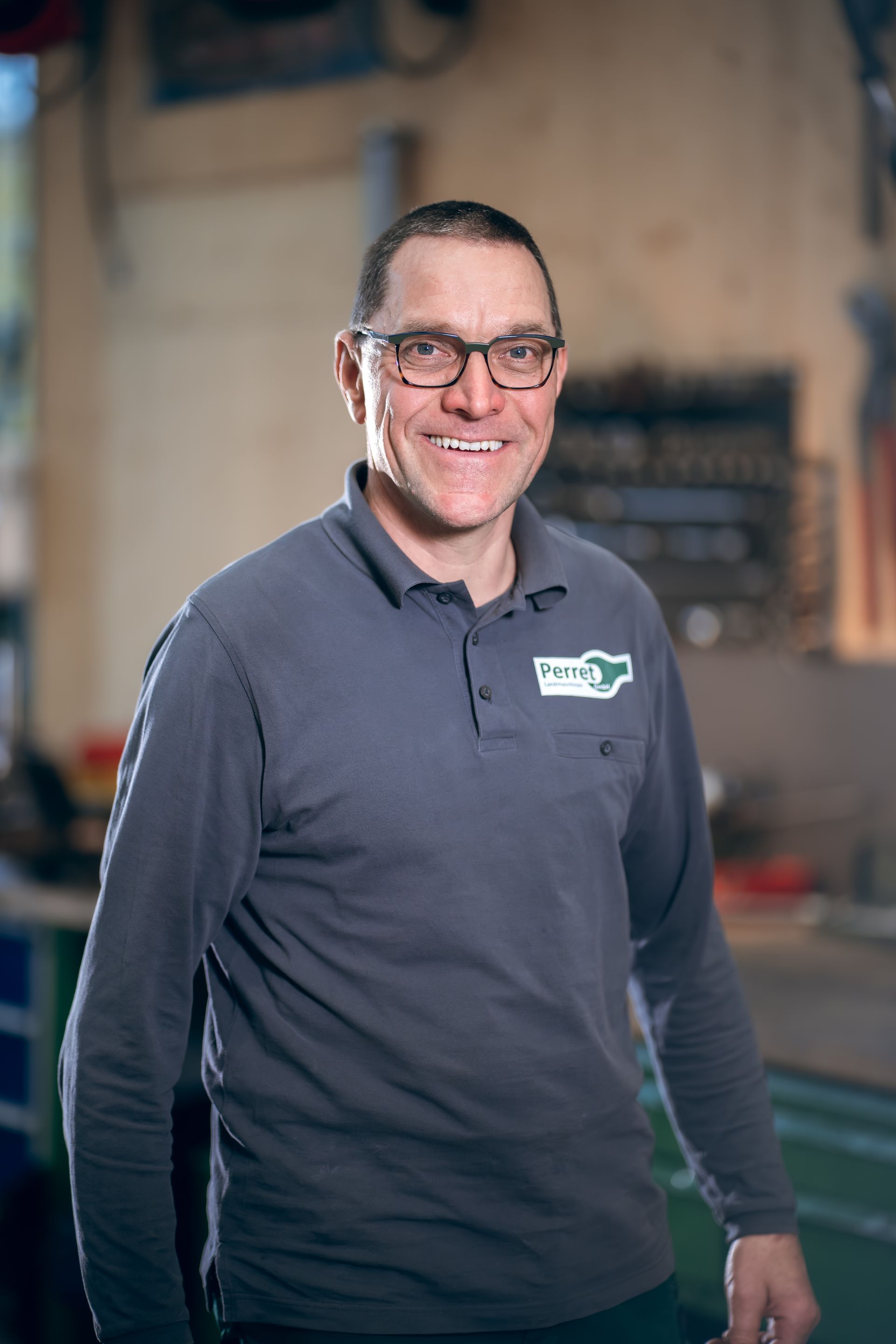 Ein Mechaniker arbeitet in einer Werkstatt an einem orangefarbenen Traktor und liegt dabei auf dem Boden.