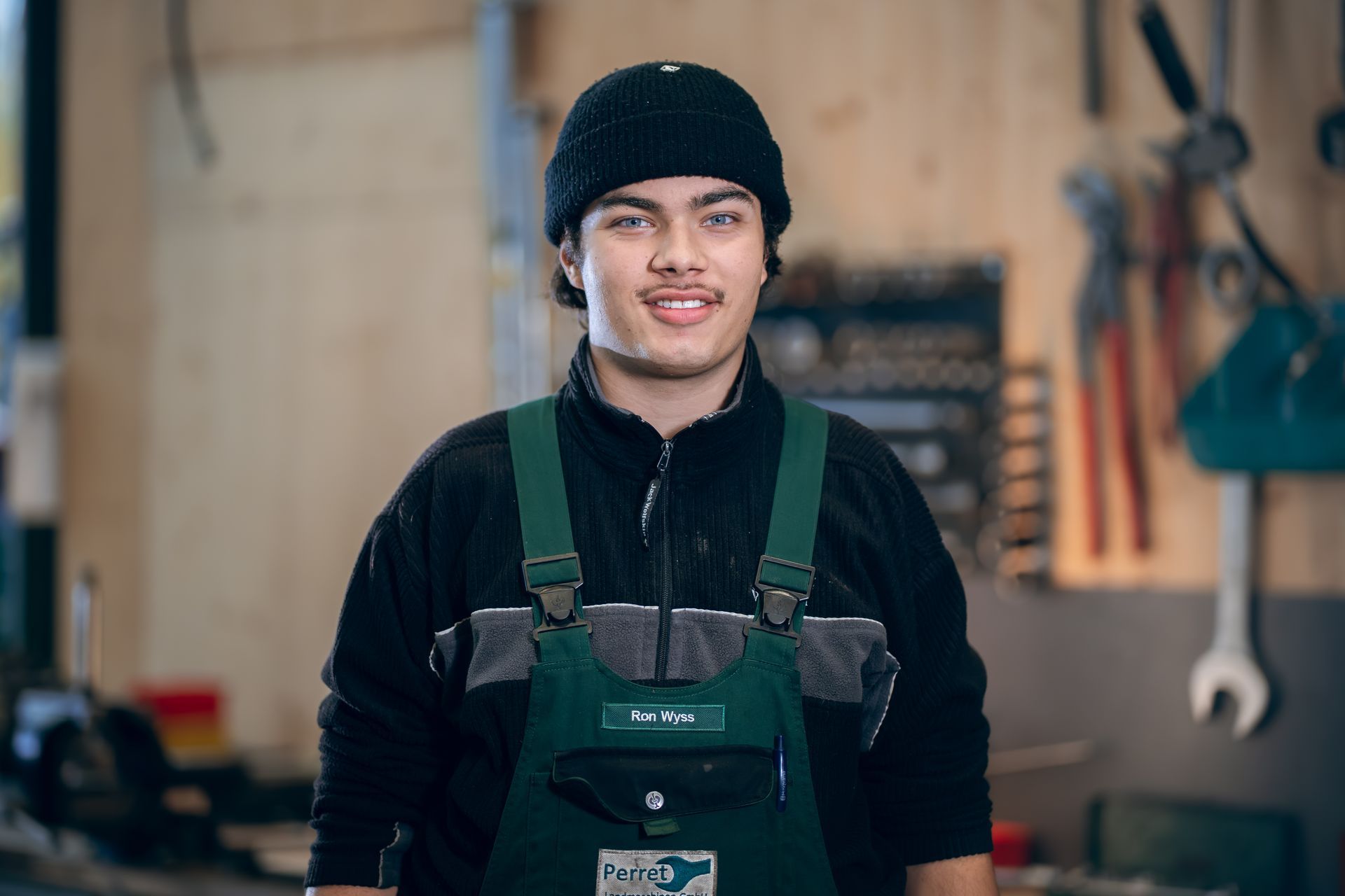 Ein Mechaniker arbeitet in einer Werkstatt an einem orangefarbenen Traktor und liegt dabei auf dem Boden.