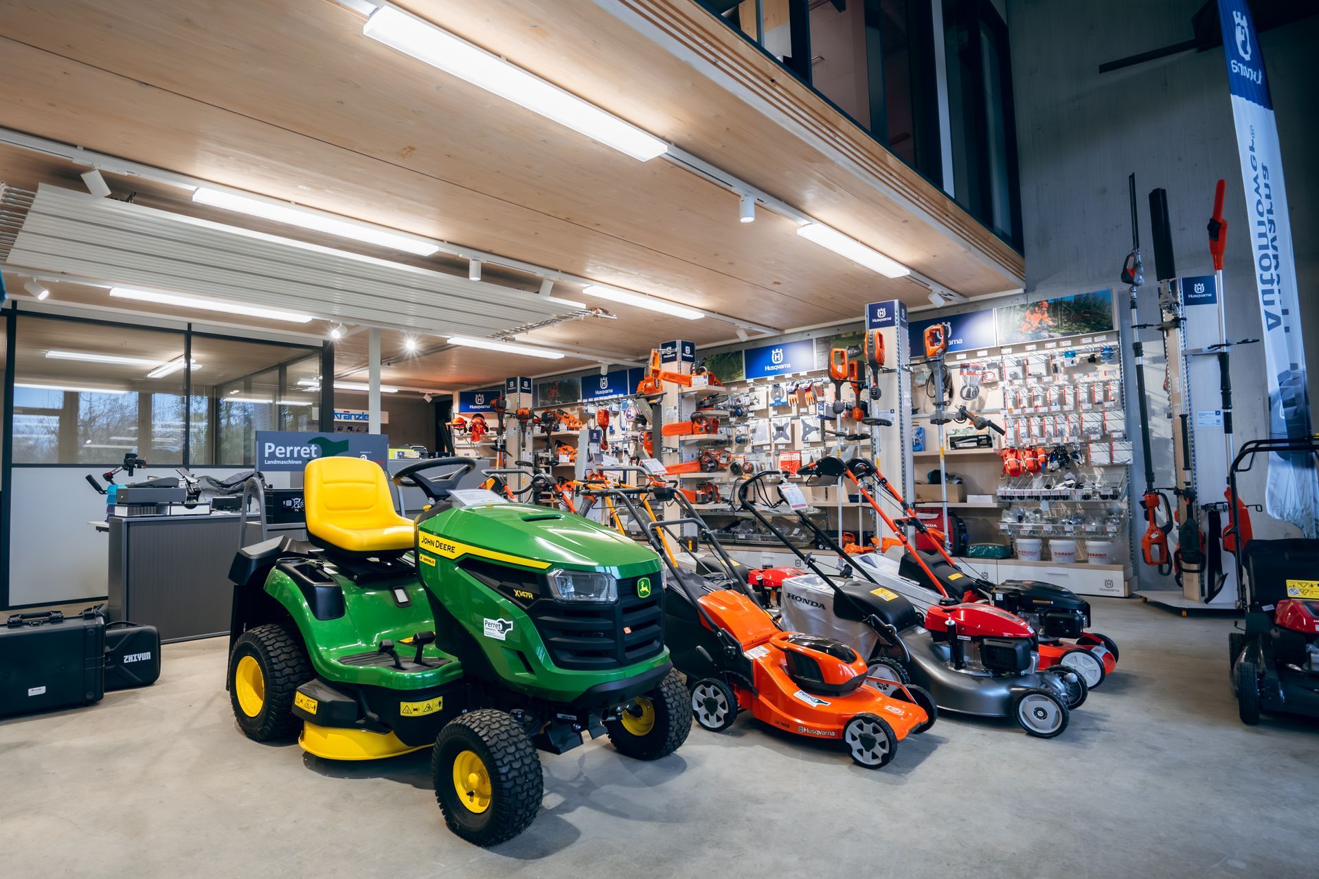 Ein grüner Traktor mäht mit einem rot-silbernen Mähwerkaufsatz ein Feld mit hohem grünen Gras.