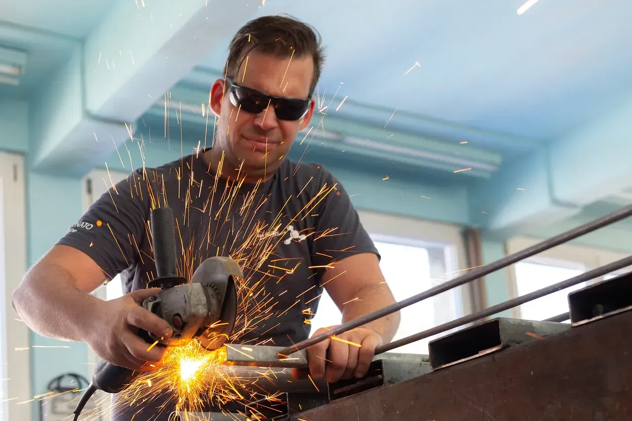 Ein Mann mit Sonnenbrille schleift ein Stück Metall.