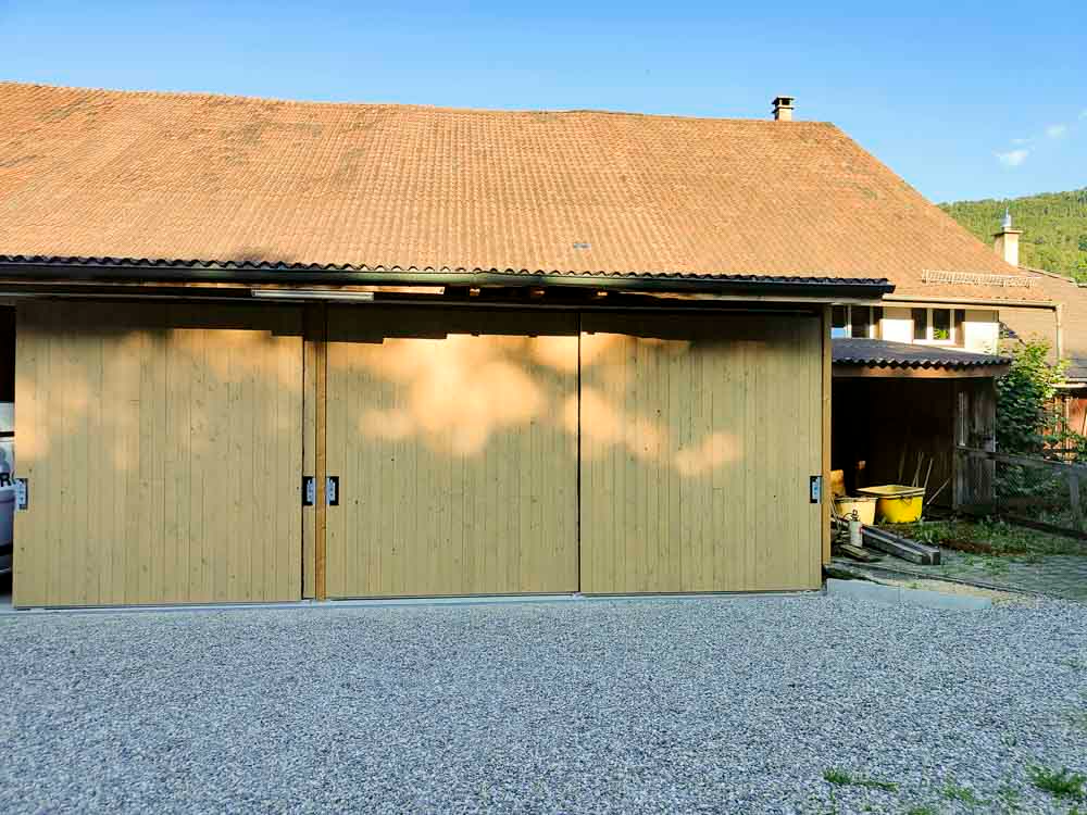 Eine Holzgarage mit Schiebetüren und einem braunen Dach