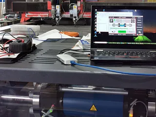 Ein Laptop steht auf einem Tisch neben einer Maschine.