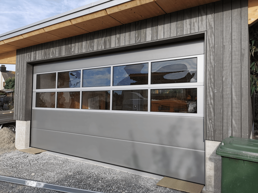 Ein Garagentor mit vielen Fenstern und einer grünen Mülltonne davor.