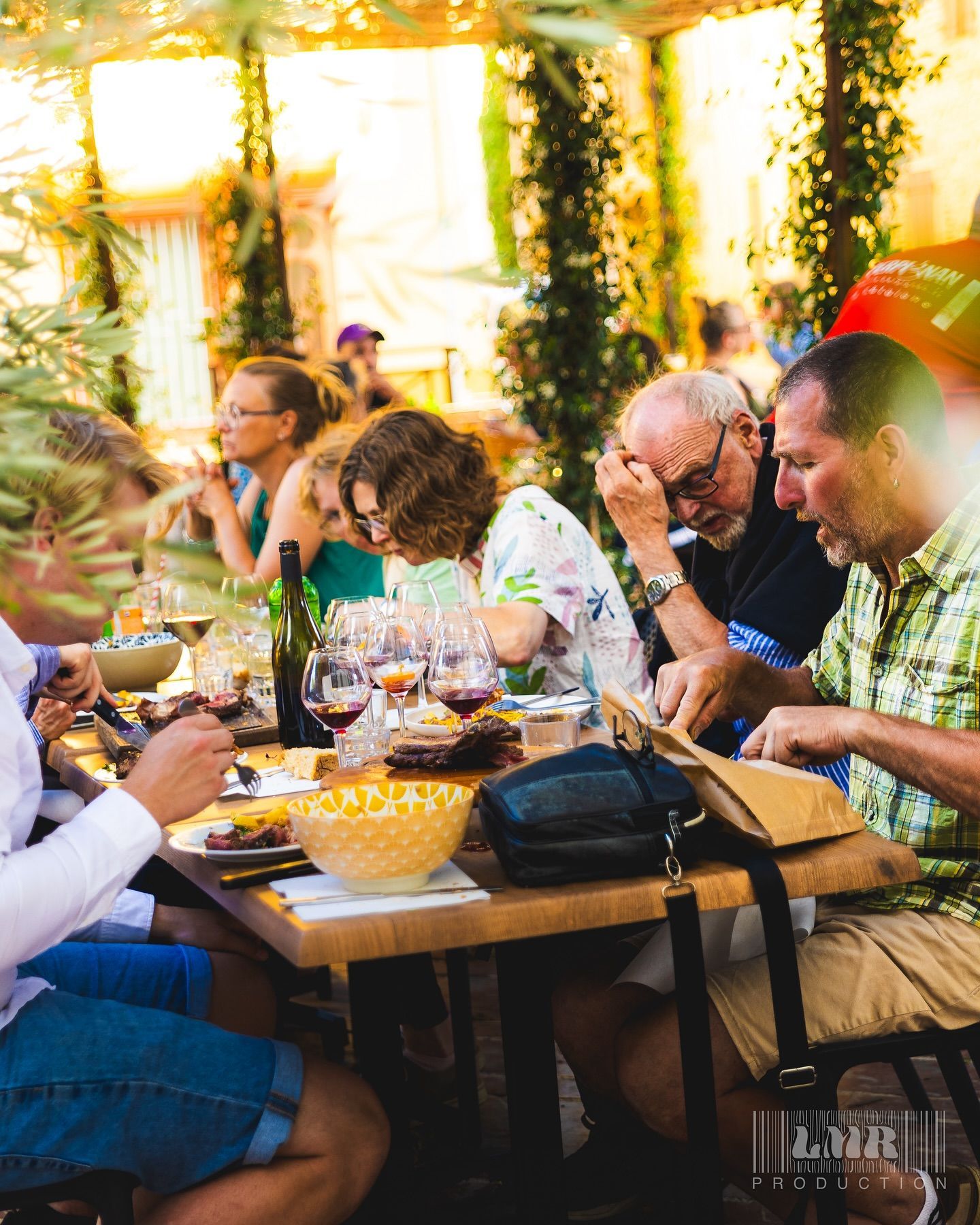 Plusieurs personnes autour d'une table de restaurant en extérieur, avec des assiettes et des verres de vin
