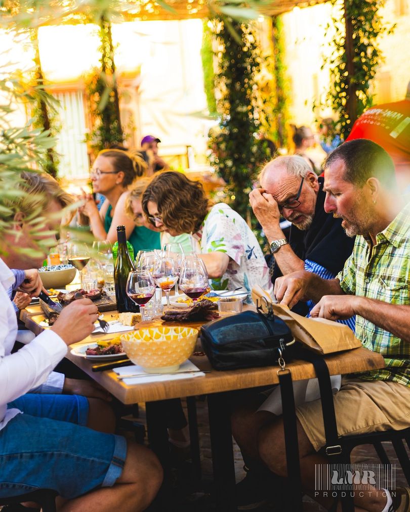 Plusieurs personnes autour d'une table de restaurant en extérieur, avec des assiettes et des verres de vin