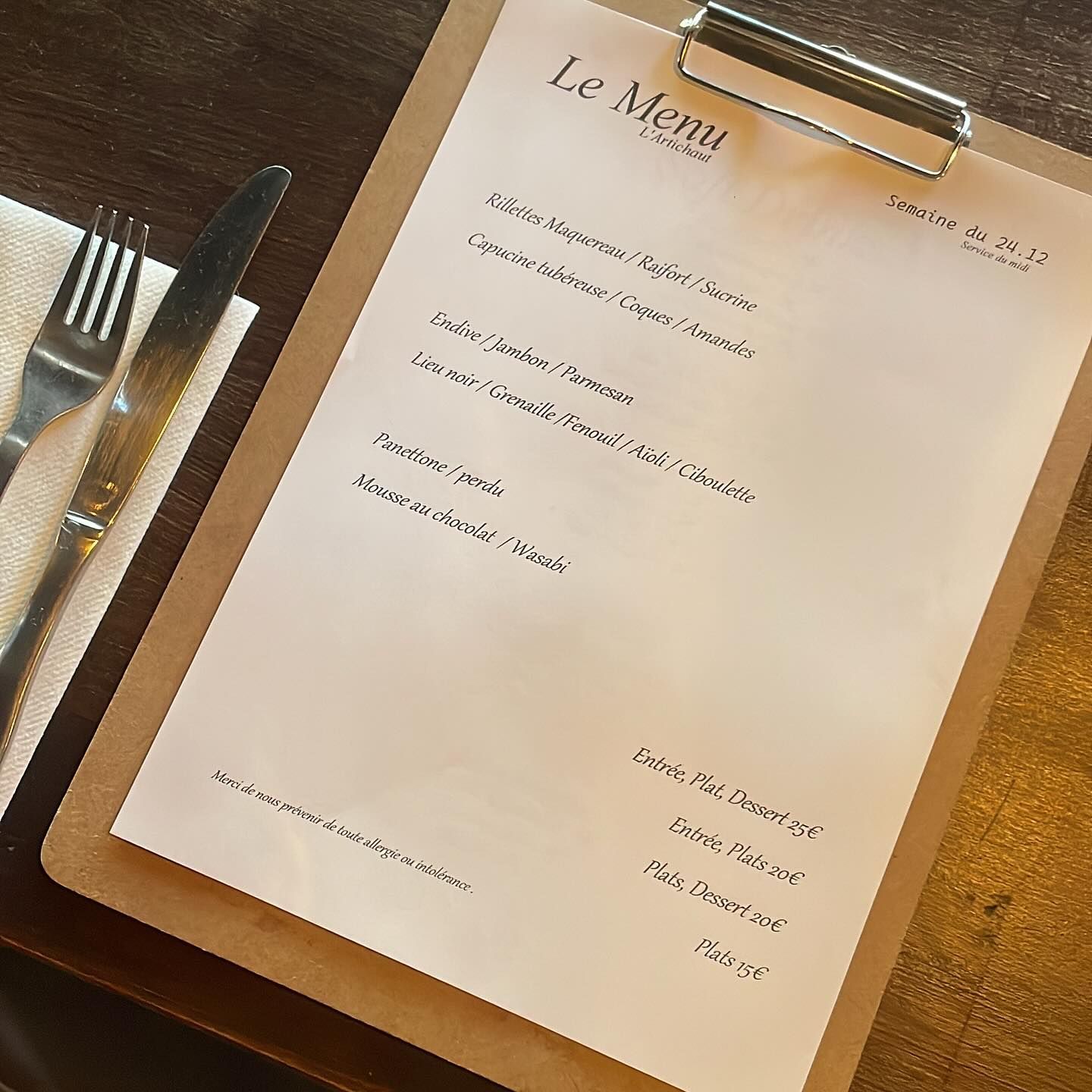 Menu de la semaine posé sur une table en bois à côté d'une fourchette et d'un couteau