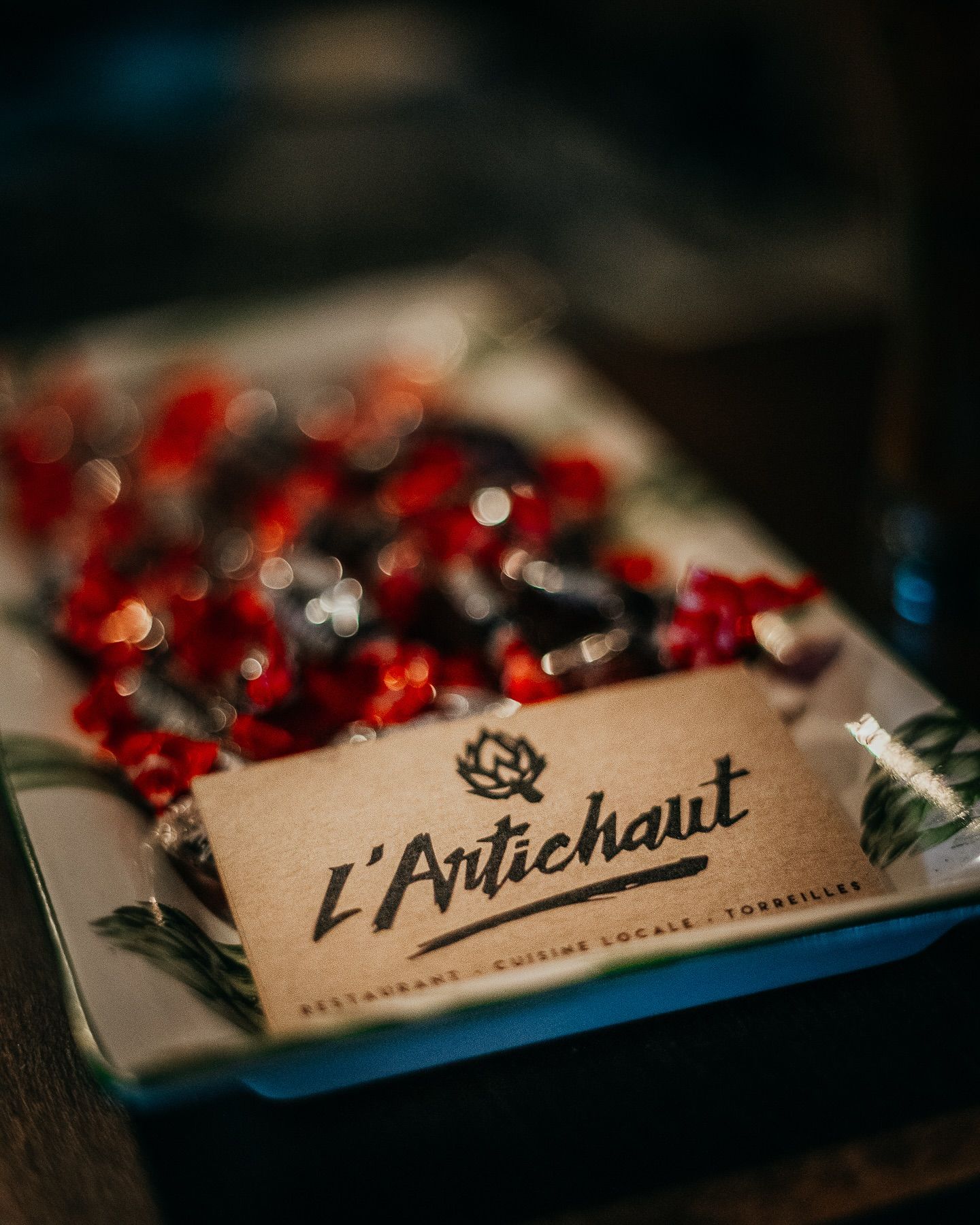 Une carte de visite du restaurant L'Artichaut, posée sur un plateau de bonbons rouges emballés