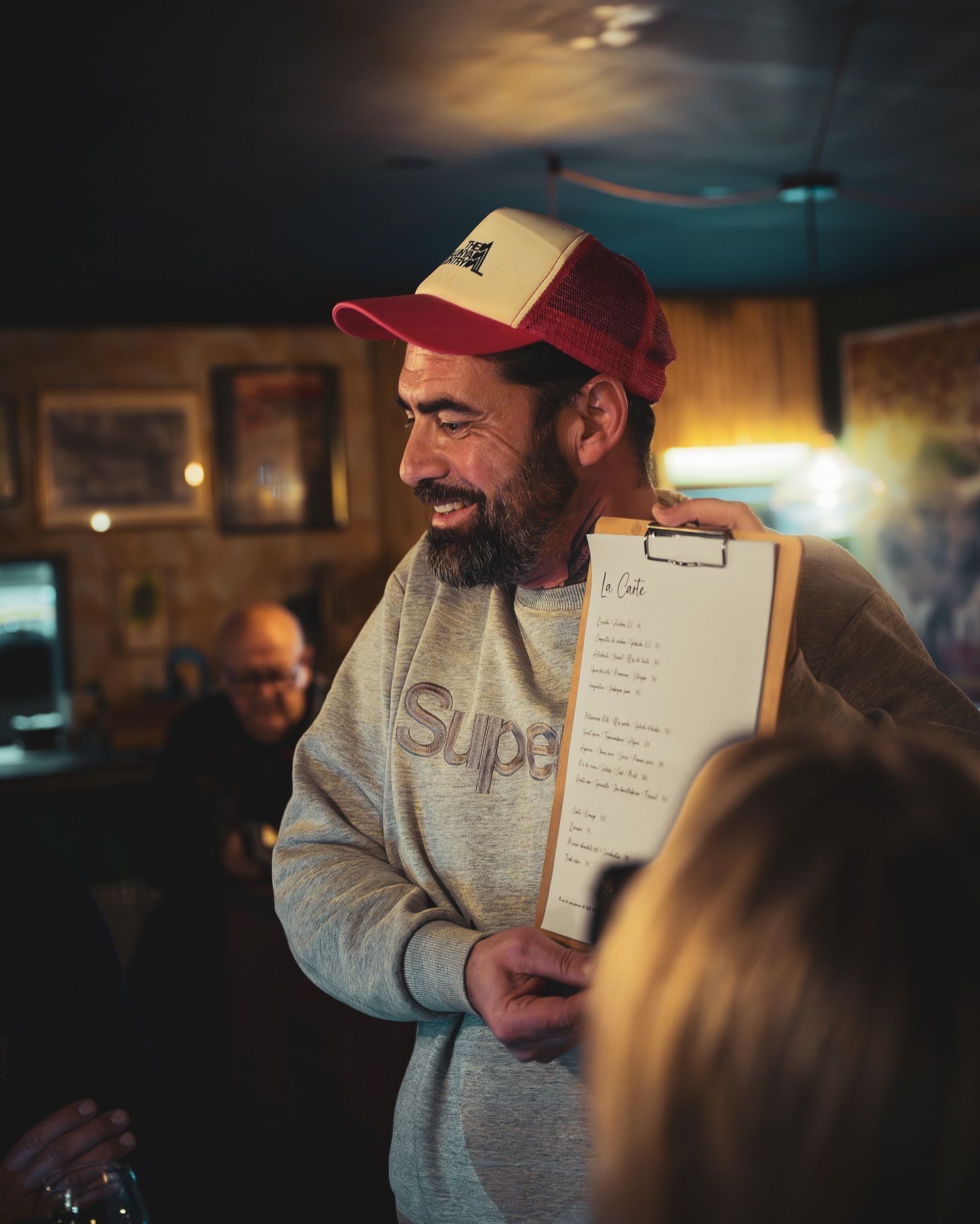Une personne souriante, coiffée d'une casquette rouge et blanche, brandit un menu à la vue de tous