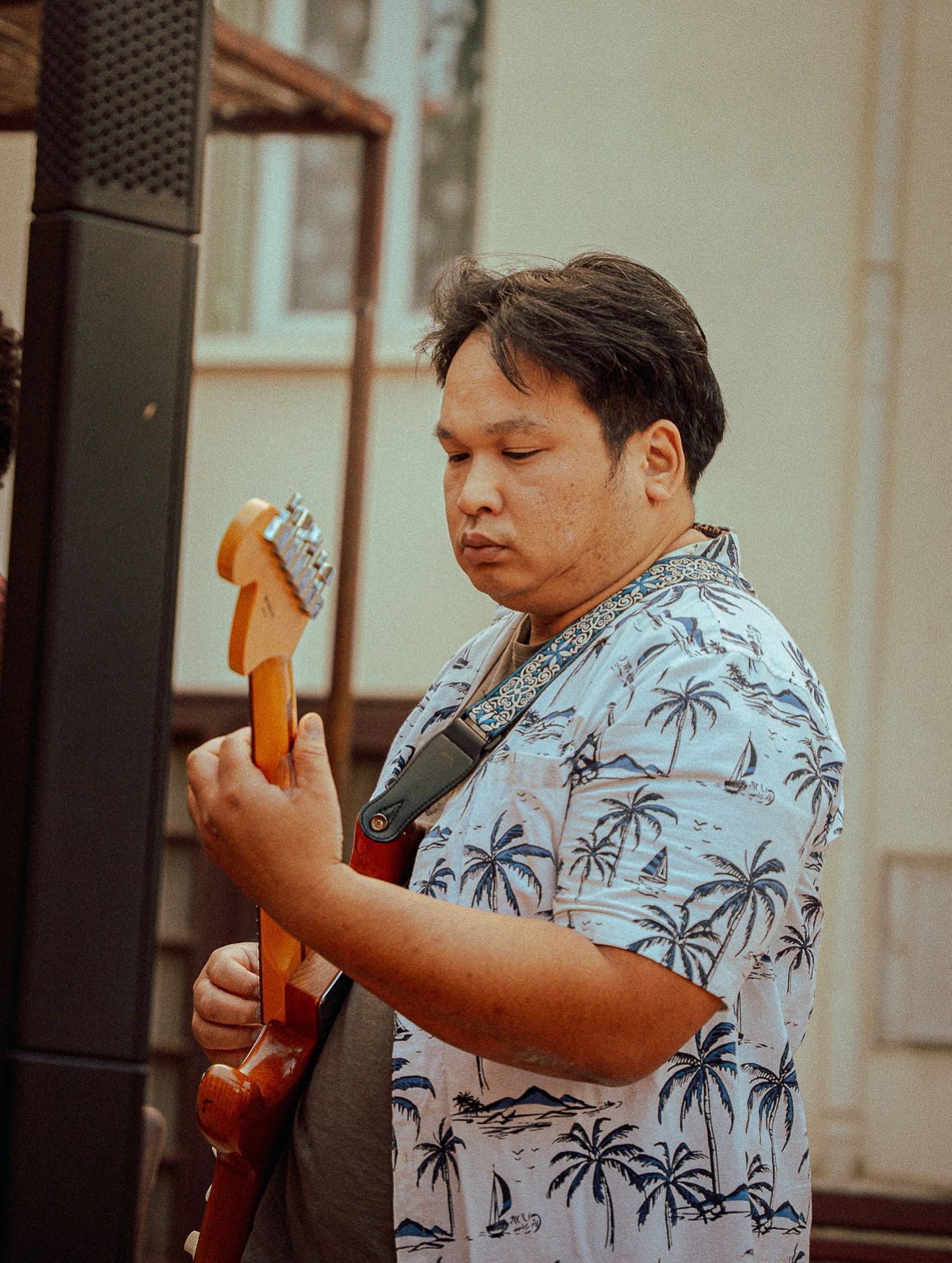 Un musicien au regard concentré joue de la guitare électrique, vêtu d'une chemise blanche à motifs de palmiers