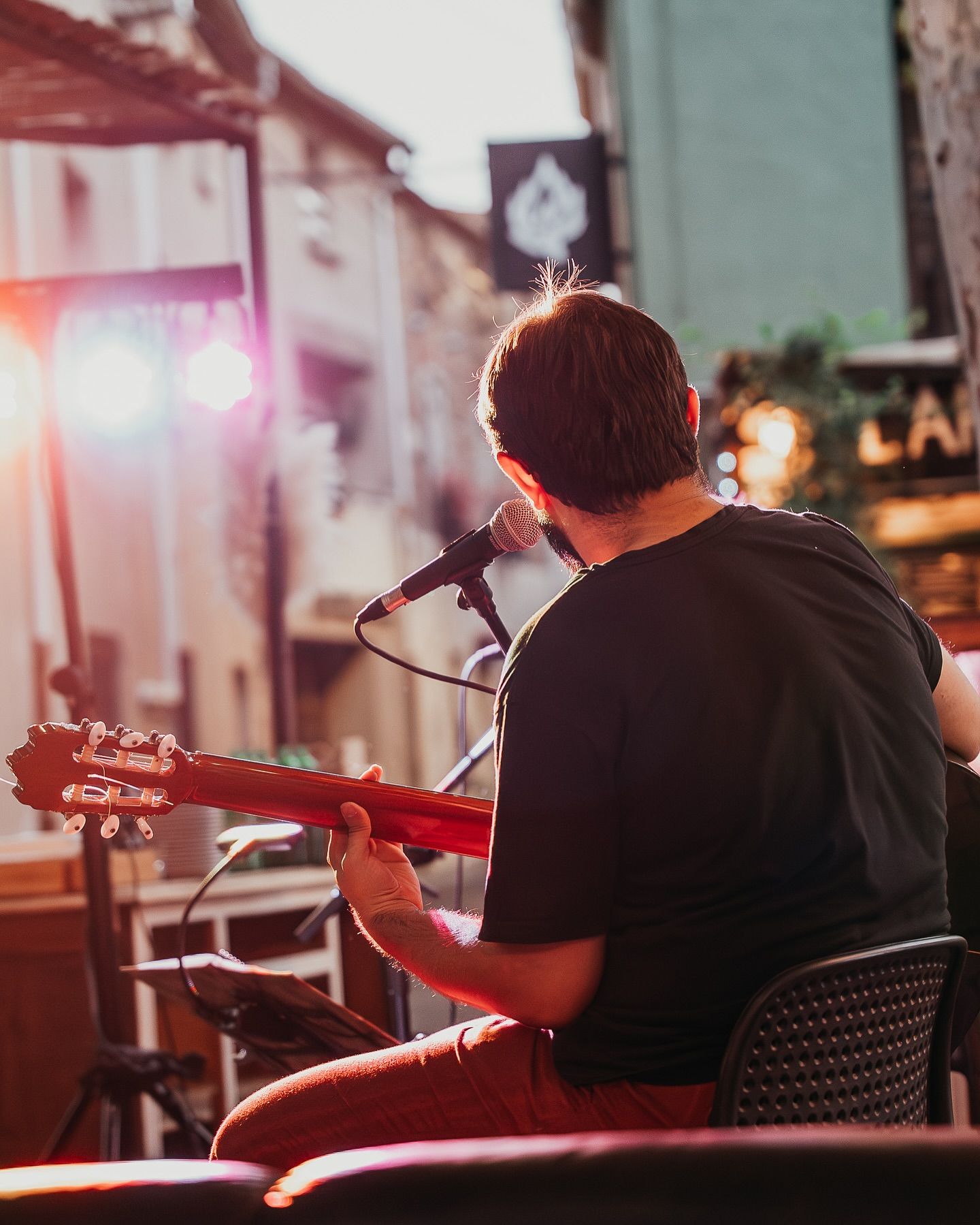 Un musicien assis sur une chaise, jouant de la guitare acoustique face à un microphone lors d'un concert en plein air en soirée