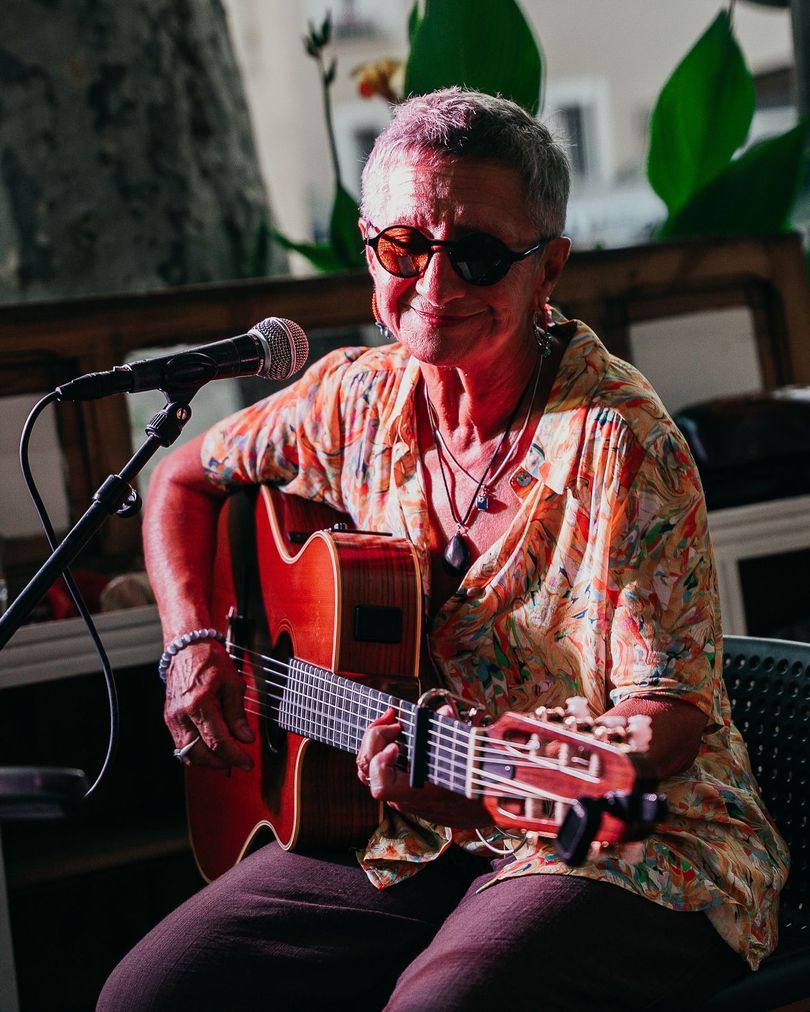 Femme avec des lunettes en train de jouer de la guitare en face d'un micro