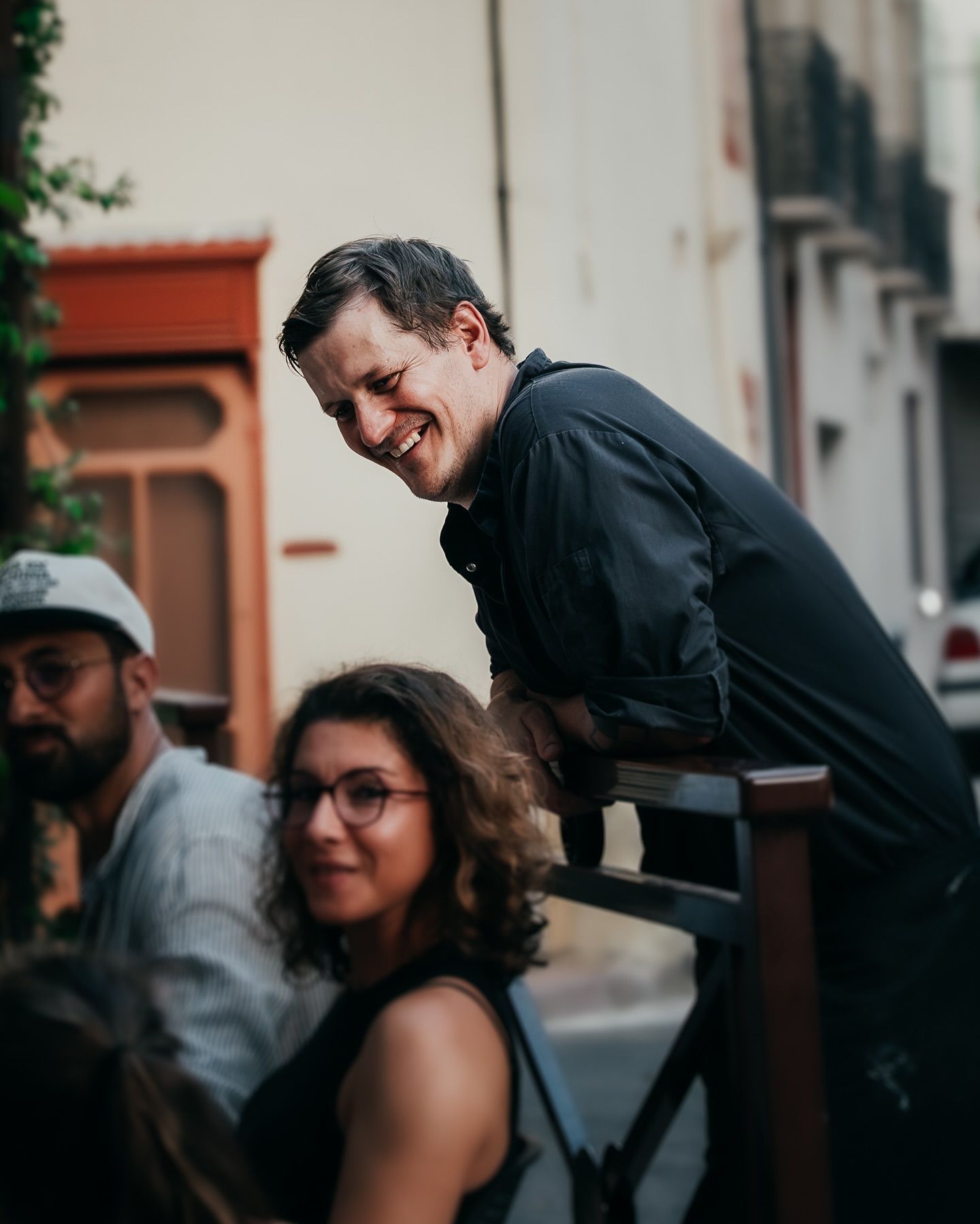 Chef du restaurant parlant à des clients sur la terrasse, appuyé sur la rambarde en bois