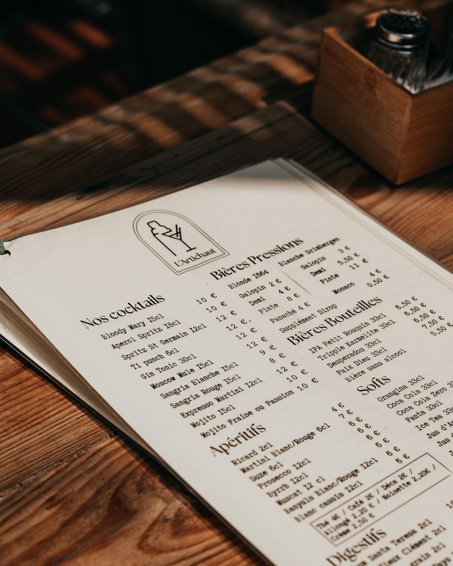 Un menu posé sur une table en bois, comportant des sections pour les cocktails, les spiritueux et les digestifs.