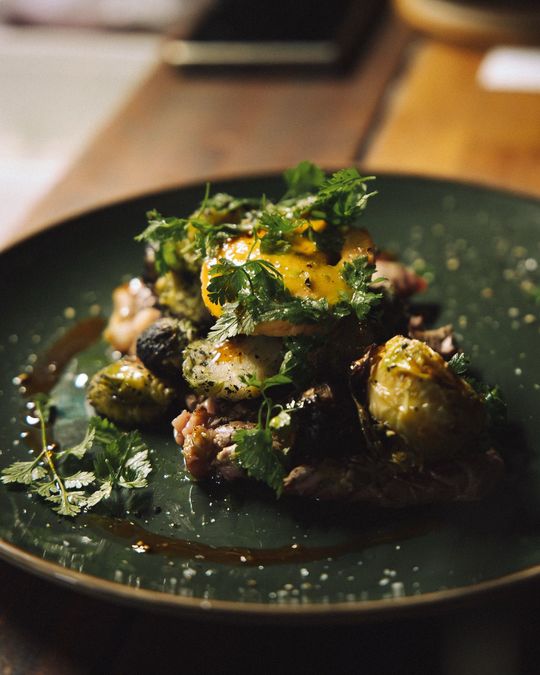 Un plat gastronomique de choux de Bruxelles rôtis, nappés d'un jaune d'œuf coulant et d'herbes fraîches, présenté sur une assiette en céramique vert foncé